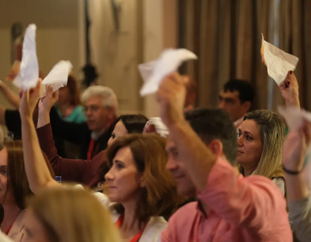 Plateia de um evento, várias pessoas com folhas de papel amarrotadas levantadas no ar ao mesmo tempo.